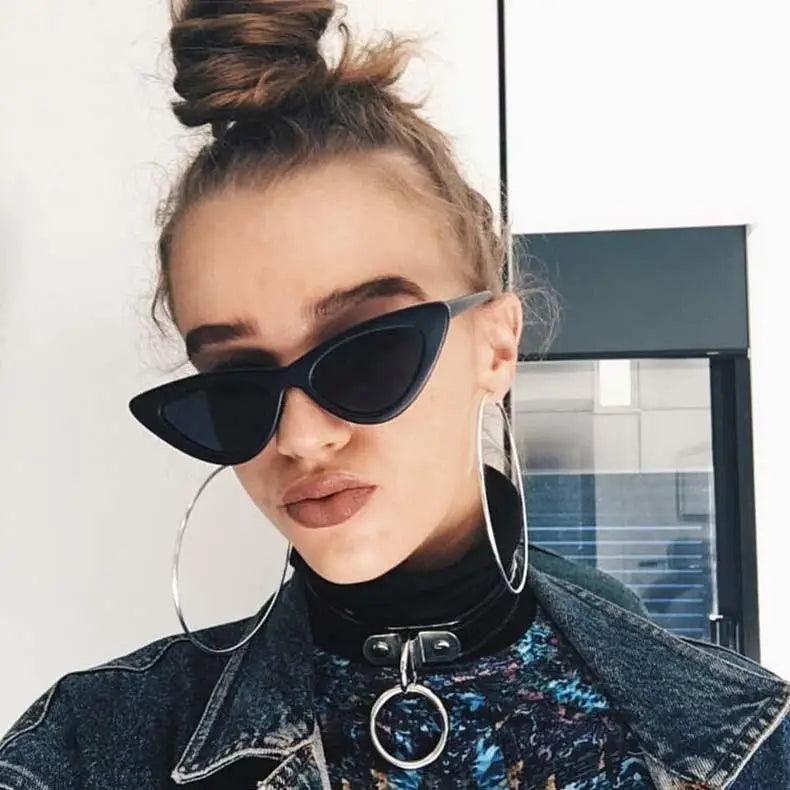 Woman wearing black cat-eye sunglasses and hoop earrings indoors.